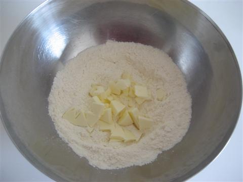 aggiungere lo zucchero e il burro (tenuto precedentemente a temperatura ambiente) tagliato a pezzettini. Mescolare con un cucchiaio gli ingredienti ottenendo così un impasto sabbioso.